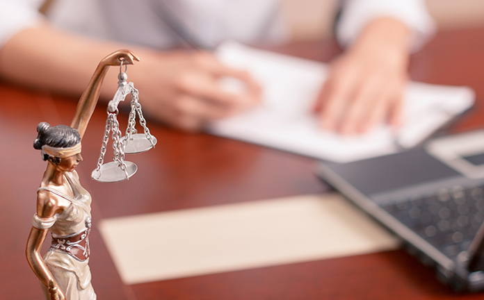 Afbeelding van vrouwe justitia met op de achtergrond iemand die formulieren invult