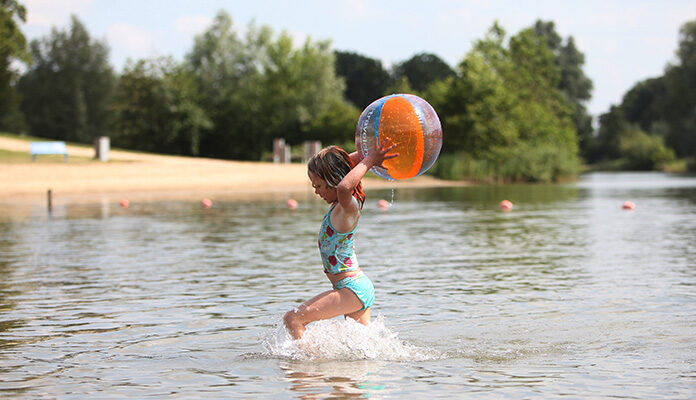 Klein meisje speelt met een bal in natuurwater.