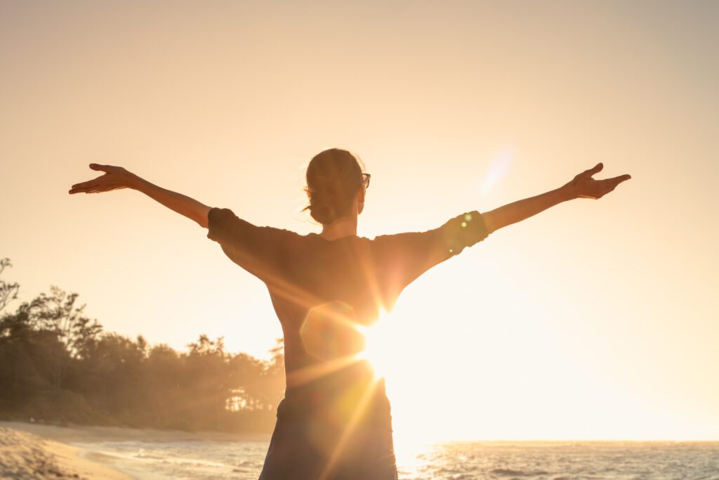 Vrouw die met haar armen wijd naar de zon gewend staat