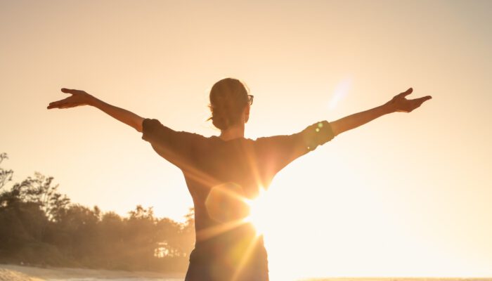 Vrouw die met haar armen wijd naar de zon gewend staat